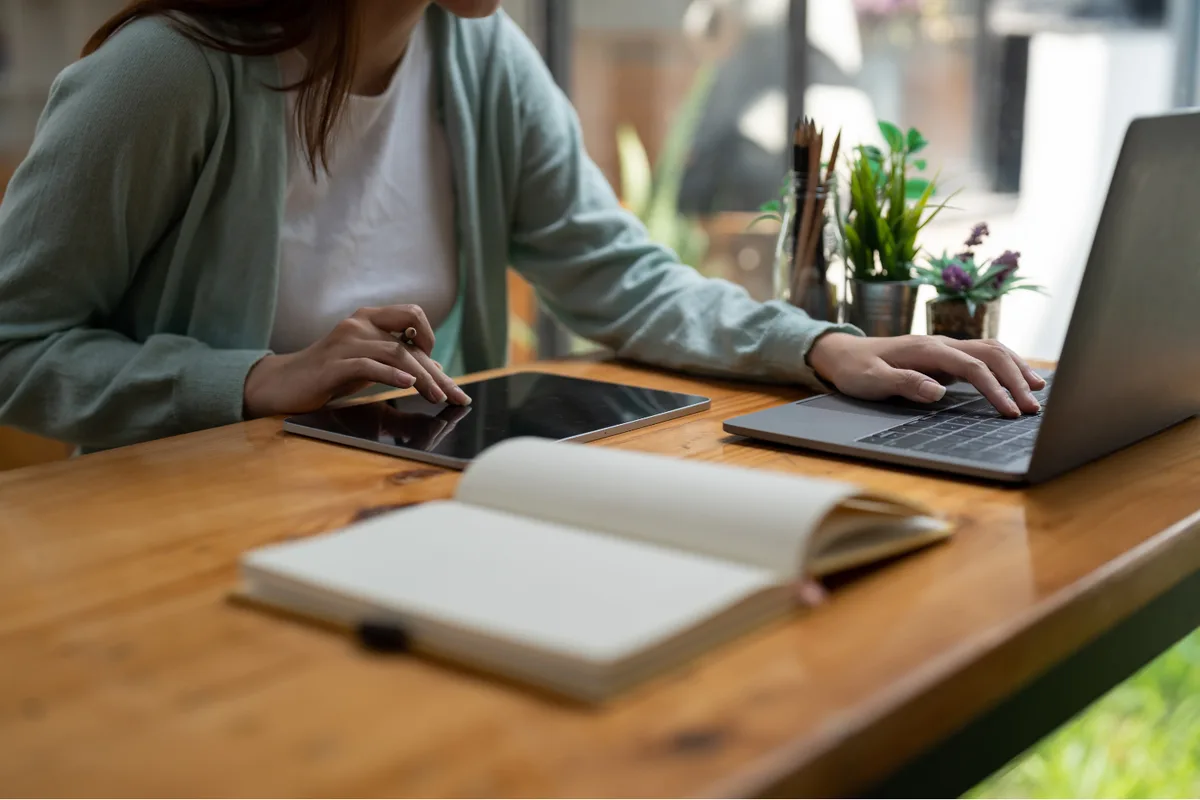 A student working online with a laptop, tablet and notebook at a desk