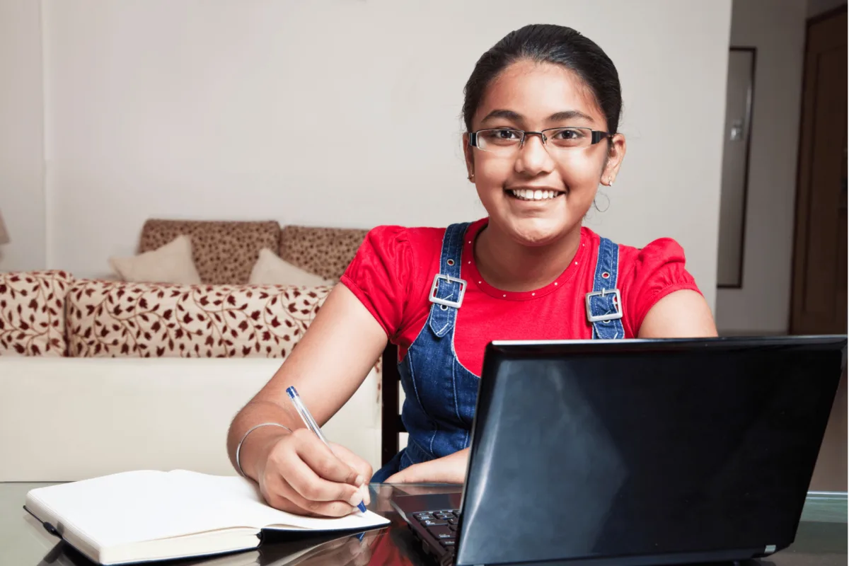 An ICSE/ISC student smiling while studying with a notebook and laptop